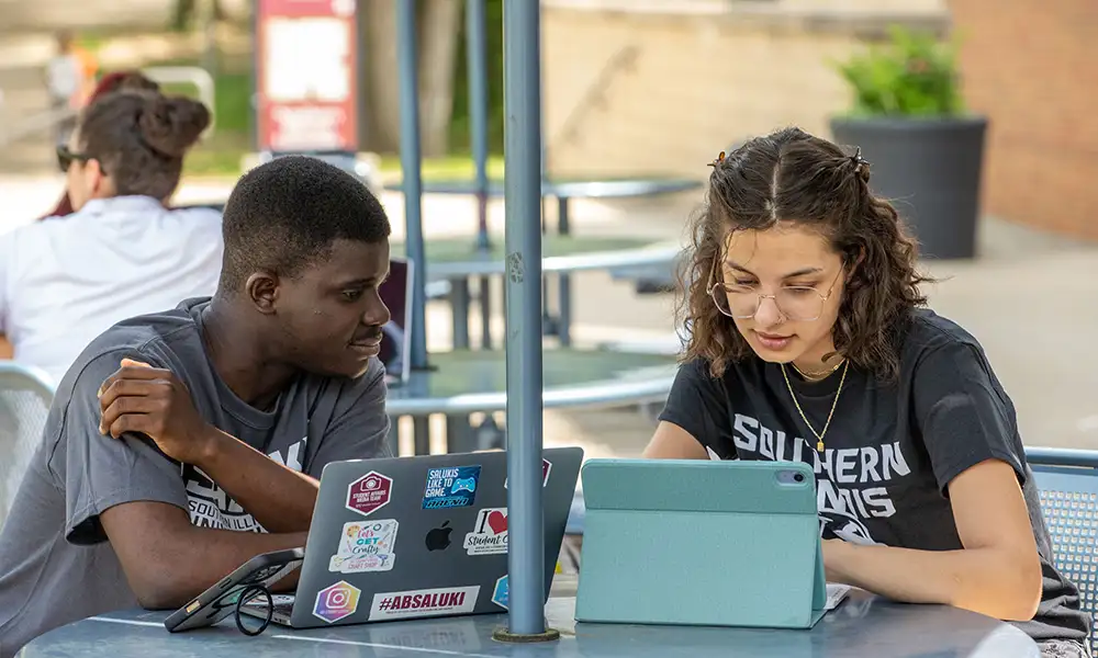 Two students studying together outdoors with laptops at Southern Illinois University.
