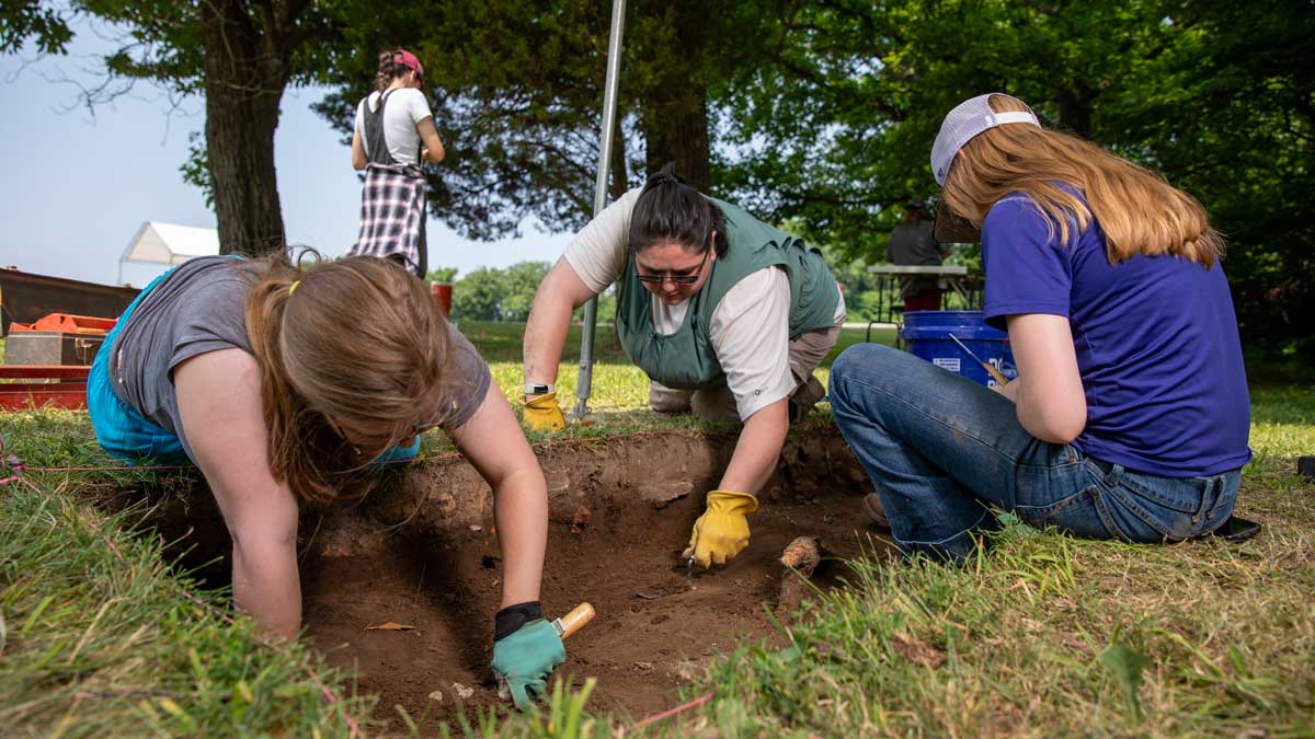 Three people excavate at an archaeological dig.