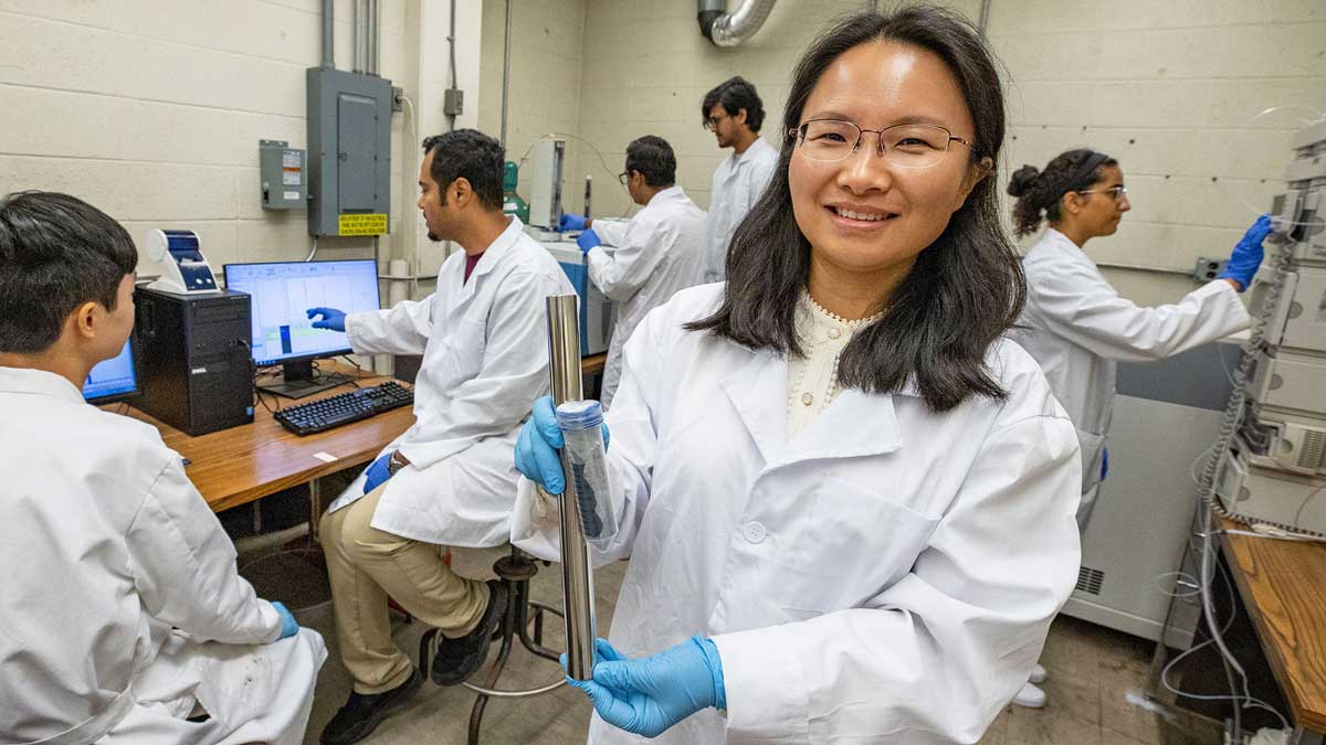 A professor holds a test tube while students work in the background.