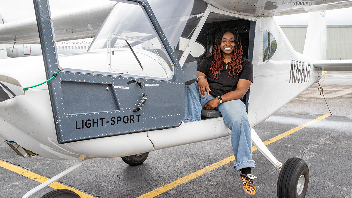 A smiling young woman sits in a small plane.