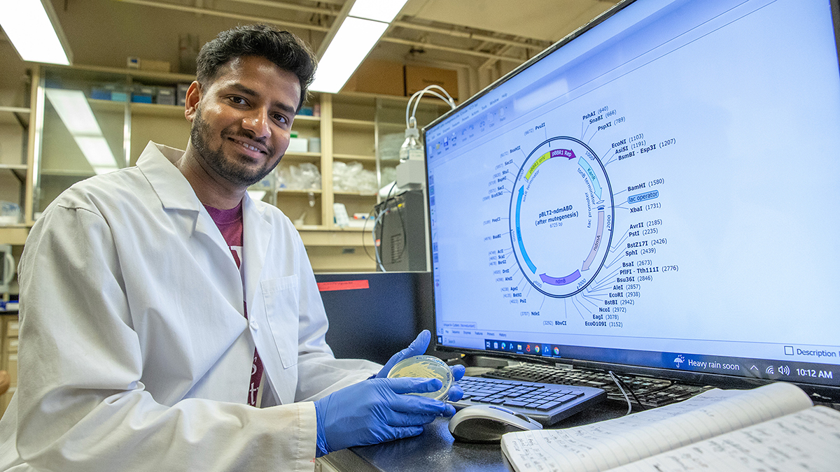 A male researcher holds a clear disc with a computer screen in the background.