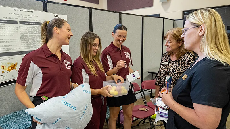 Three female students hold objects while they chat with members of the community.