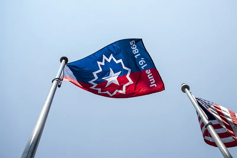 A Juneteenth flag waves in the wind, with a U.S. flag nearby.