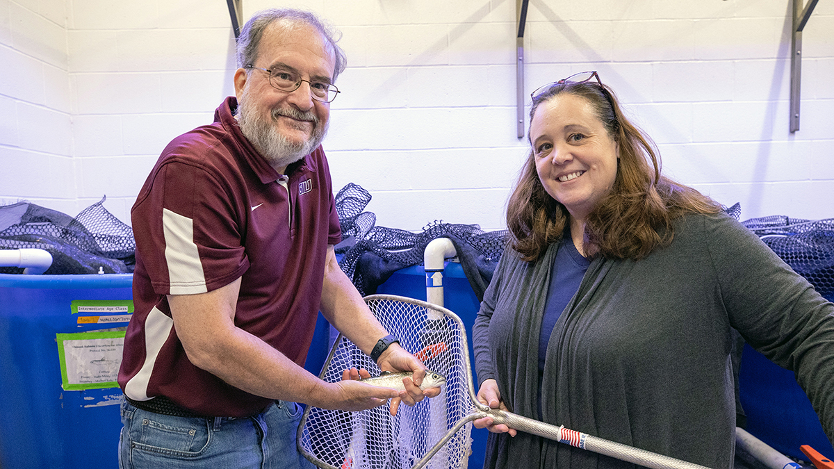 A male scientist and female scientist show off a Chinook salmon in their lab.