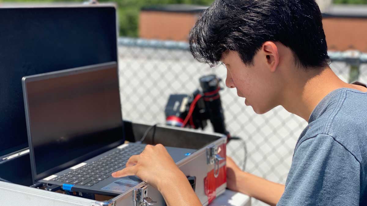 Male student at computer with telescope in the background