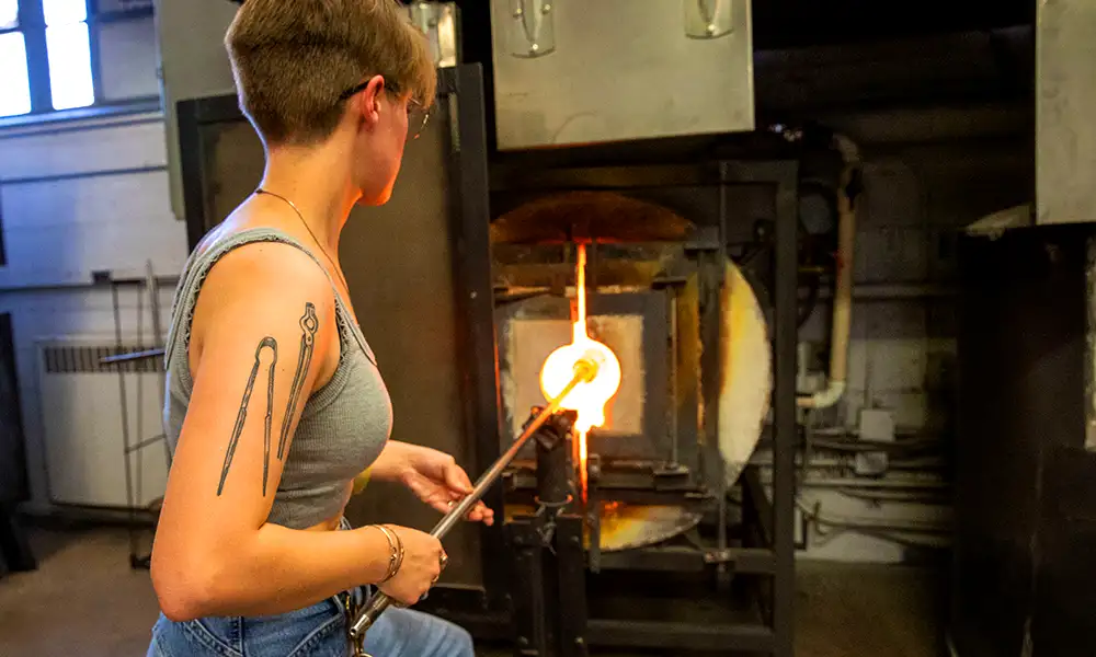 student blowing glass in studio