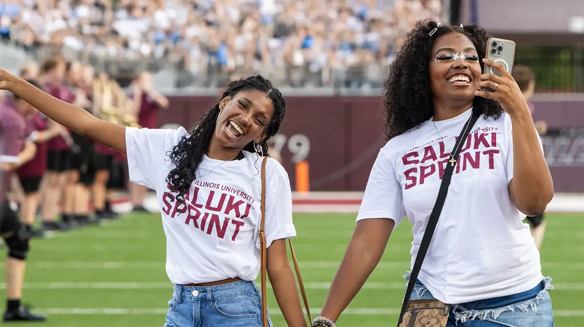 Two SIU students smiling and celebrating during the Saluki Sprint on the football field.