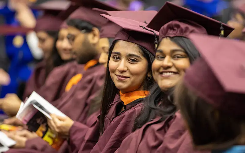 Graduates in maroon caps and gowns smile while seated in rows during the commencement ceremony at Southern Illinois University.